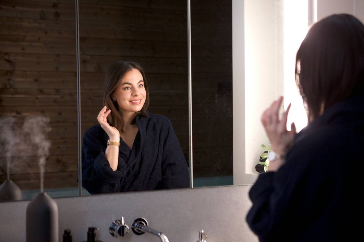 A woman in front of the mirror with her youthful-looking skin.